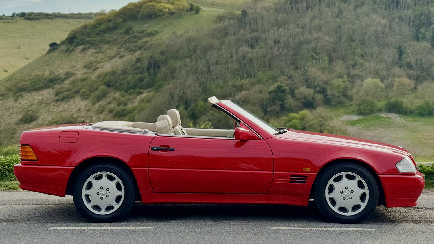 Side view of red Mercedes-Benz SL R129 convertible with roof down in countryside setting